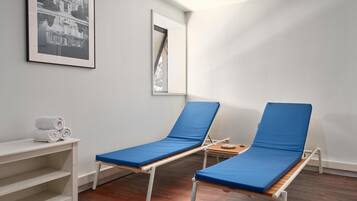 Ein Zimmer mit zwei blauen Polstersesseln, einem weißen Regal mit Handtüchern und einem gerahmten Bild an der Wand.