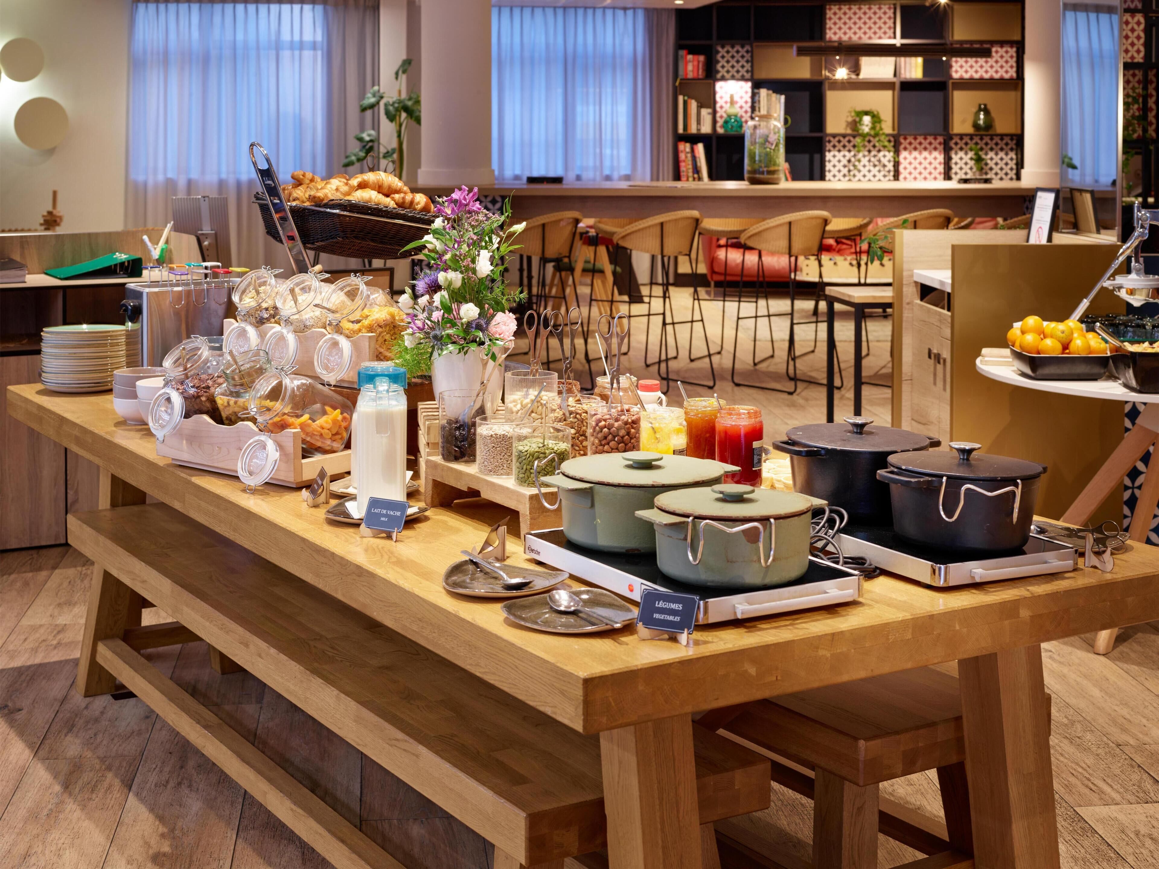 A buffet table with various food items and containers, a bookshelf in the background, and a dining area with chairs.