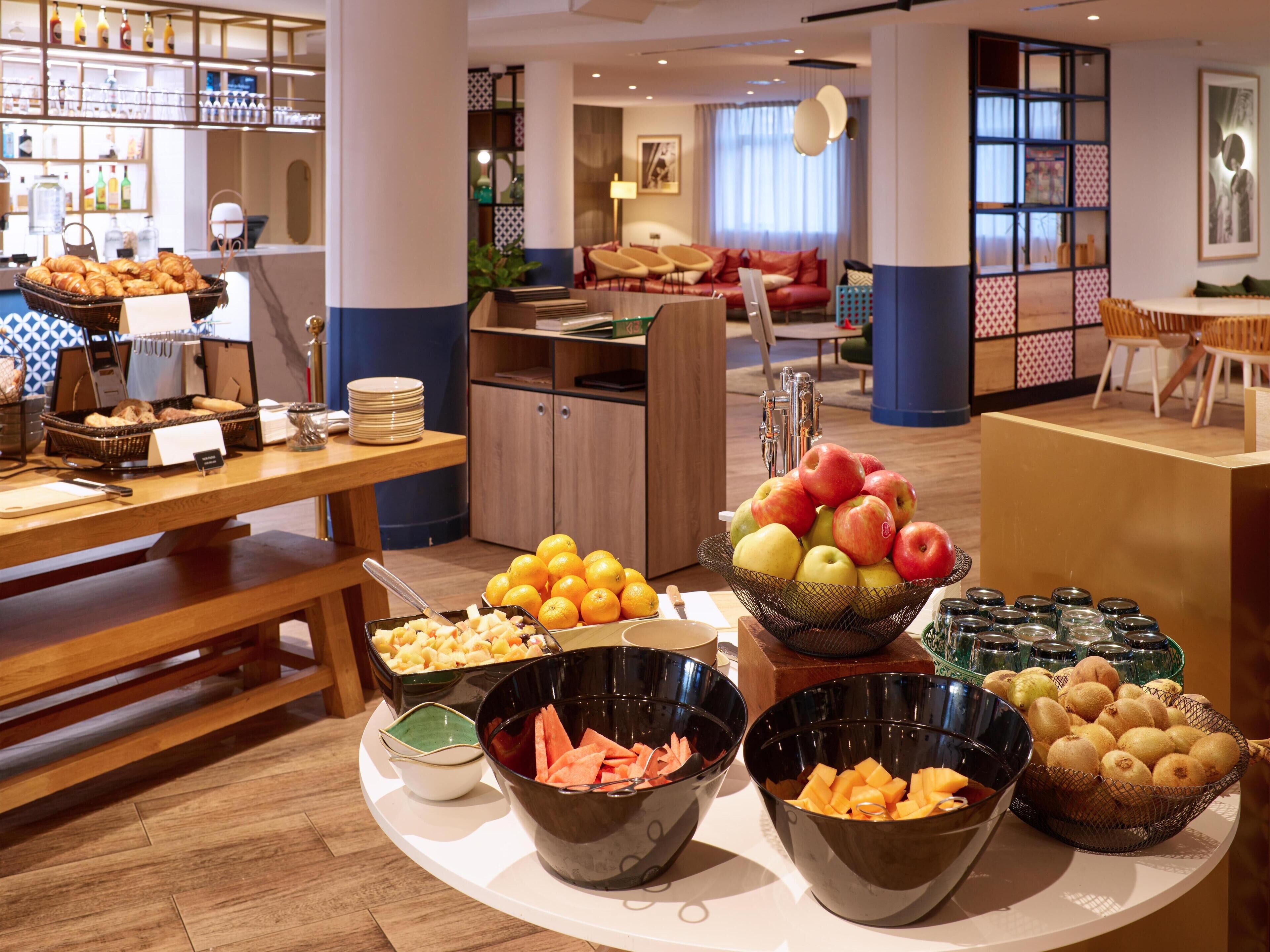 Een buffet met verschillende soorten fruit en groenten, een zithoek met een bank en stoelen, en een bar met flessen.