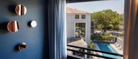 A room with a large window, a view of a swimming pool, and a building with a tiled roof.