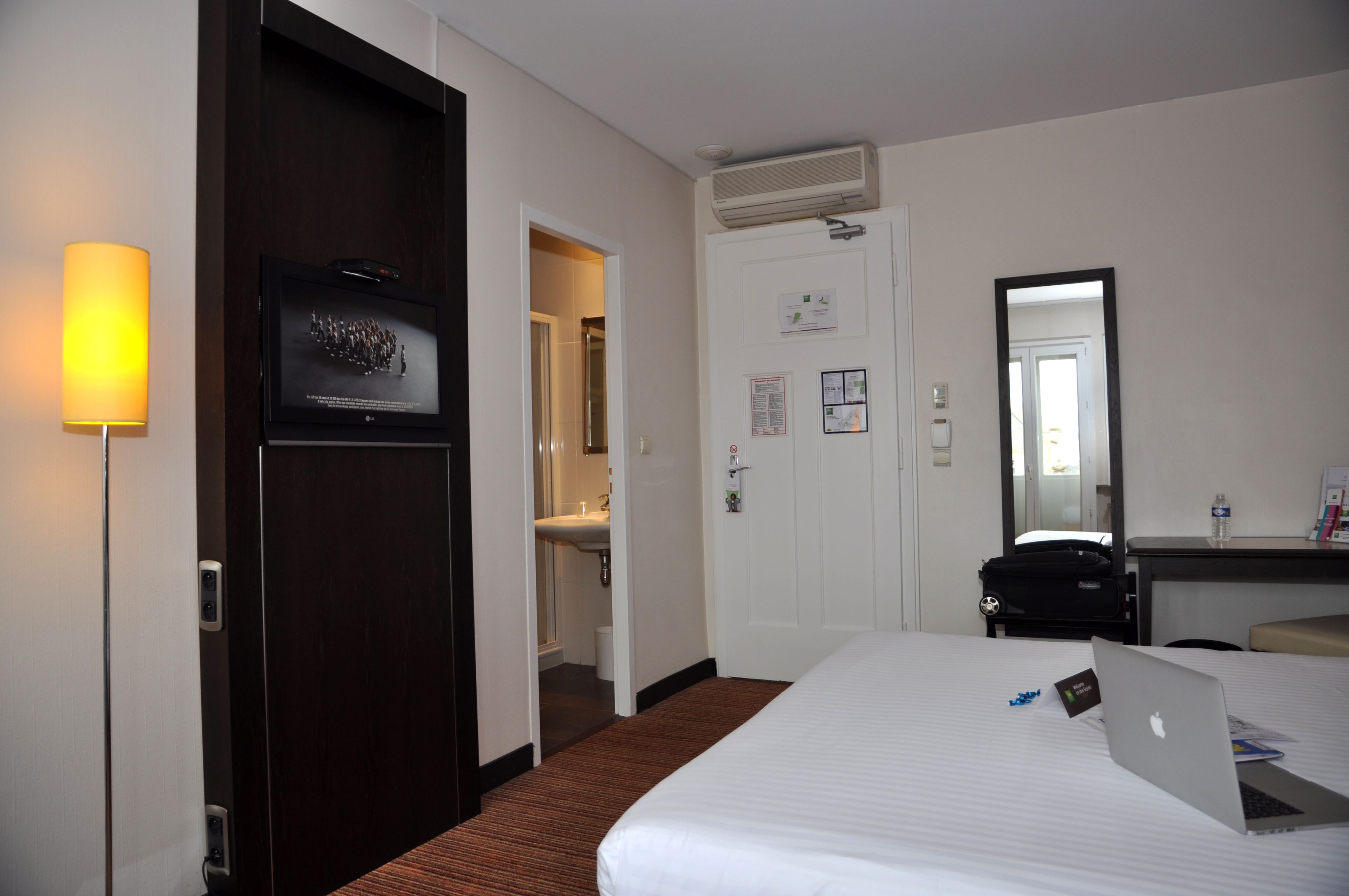 Une chambre d’hôtel comprenant un lit, un bureau avec un ordinateur portable, un miroir et une porte donnant accès à une salle de bain.