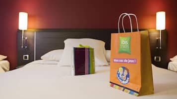 A hotel room with a bed, pillows, a nightstand, and a lamp. There is a gift bag on the bed.