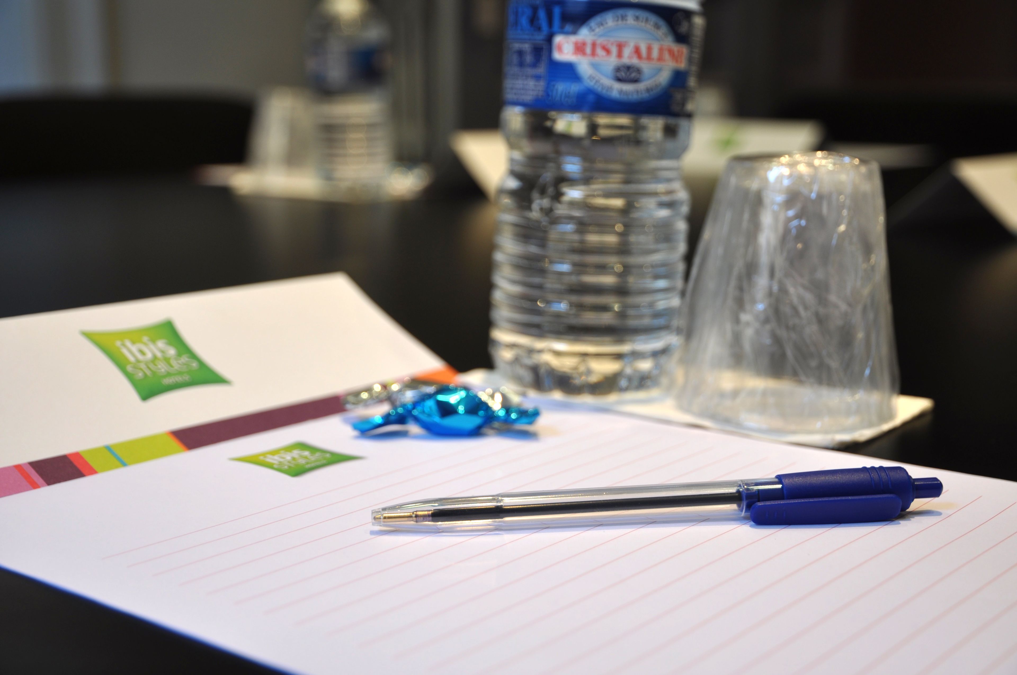 Un cuaderno con un bolígrafo, una botella de agua y un vaso sobre una mesa.