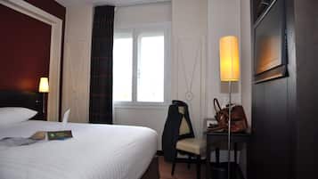 A hotel room with a bed, a desk with a lamp, a chair, a TV, and a window with curtains.
