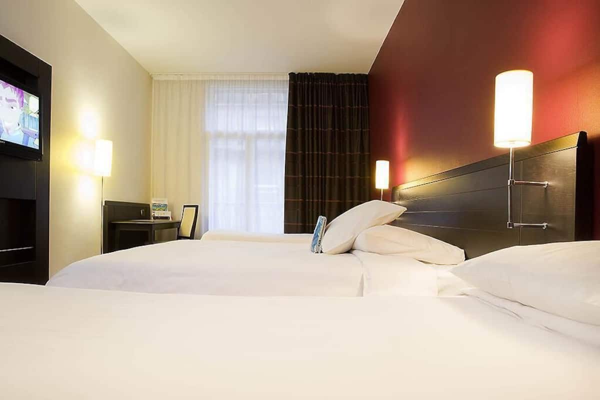 A hotel room with two beds, a TV, a bedside table, and a lamp.