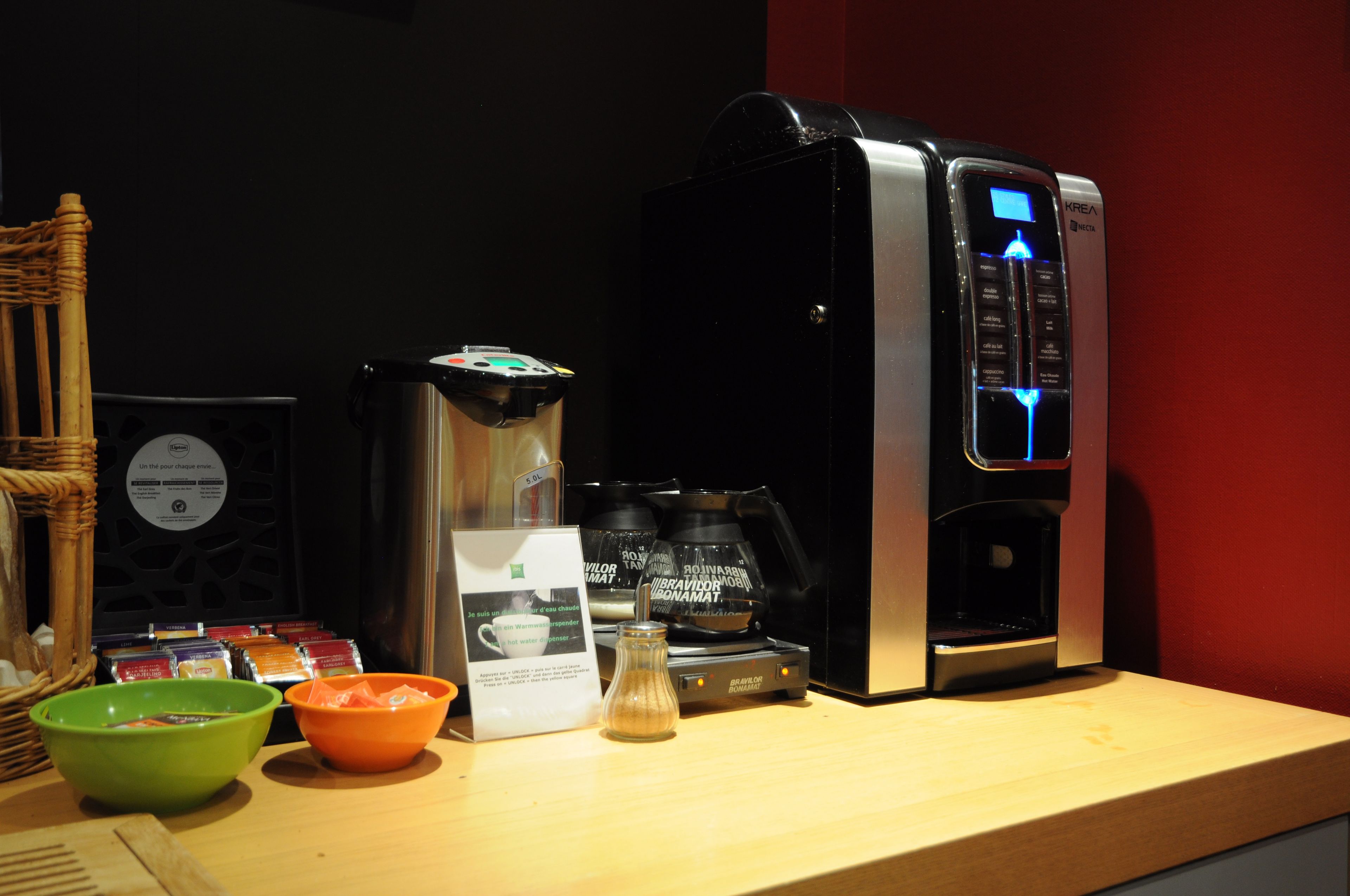 A coffee machine with a digital display, a coffee pod holder, and a small glass jar on a wooden counter.