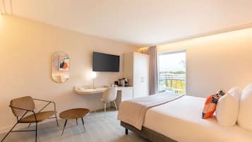 Une chambre d’hôtel équipée d’un lit, d’un bureau, d’une chaise, d’une petite table, d’un téléviseur et d’une fenêtre donnant sur un paysage agréable.