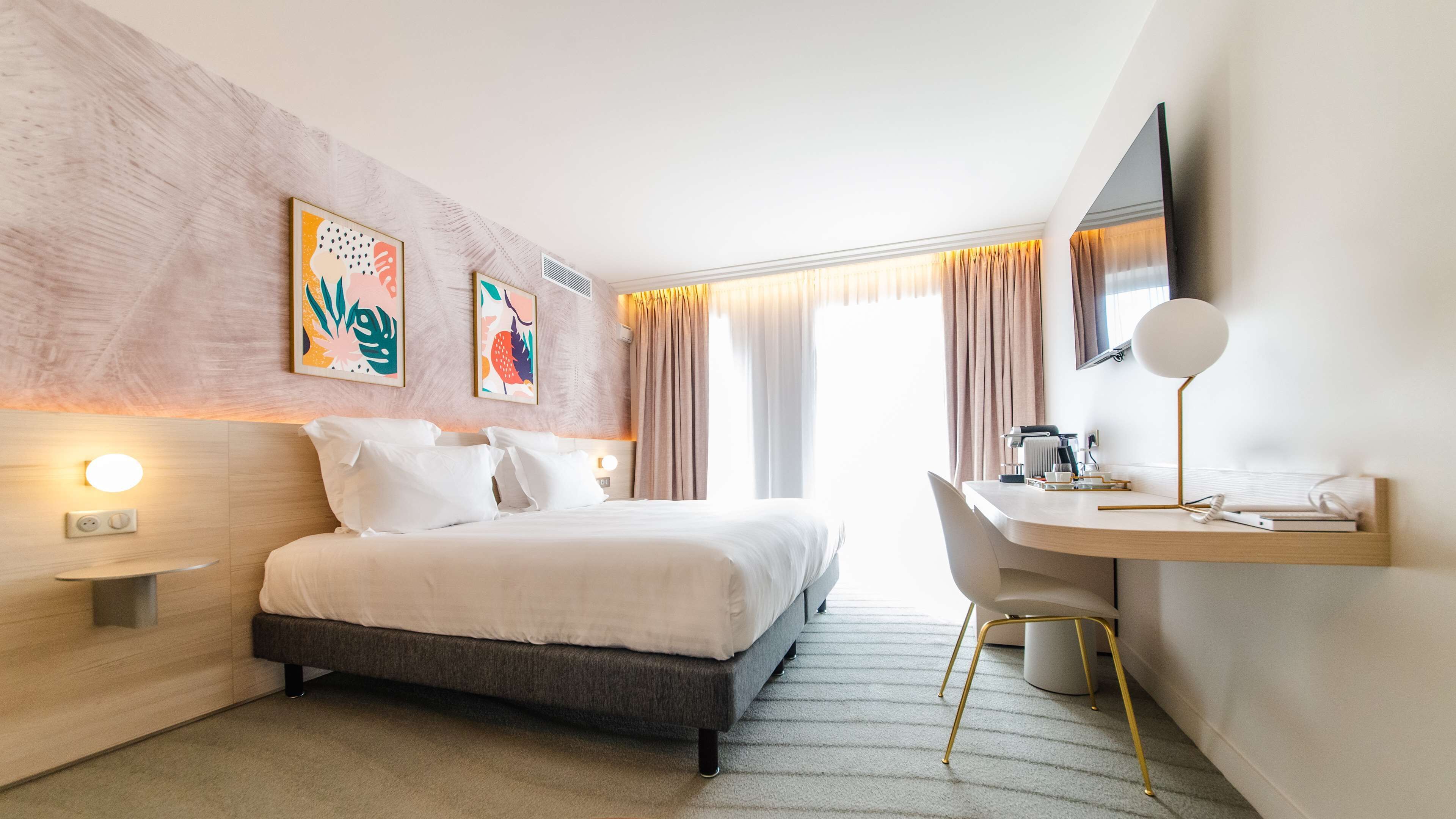 A modern hotel room with a bed, bedside table, desk, and chair.