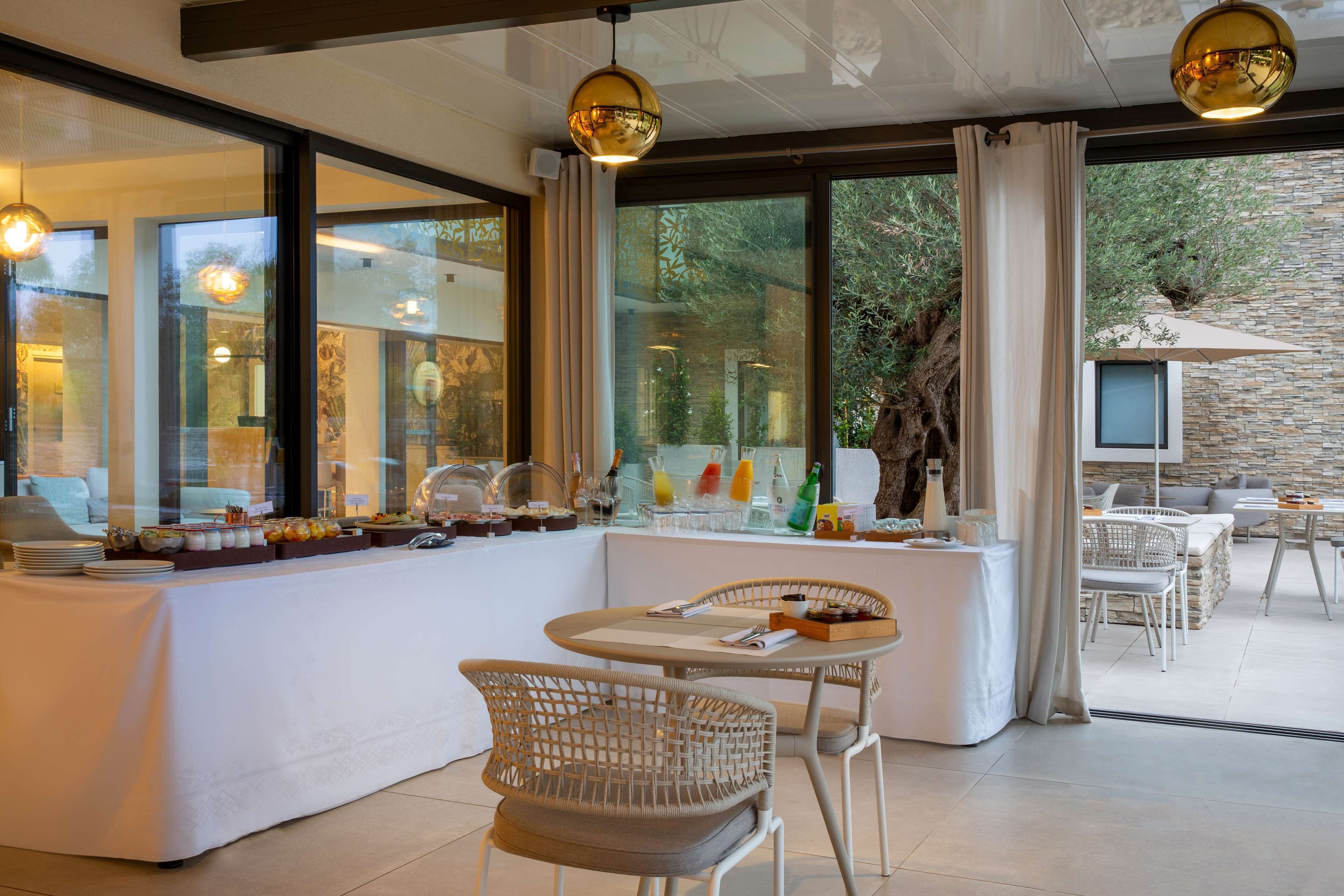 A modern dining area with a buffet setup, wicker chairs, and large windows offering a view of the outdoors.