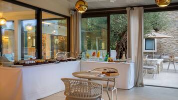 A modern dining area with a buffet setup, wicker chairs, and large windows offering a view of the outdoors.