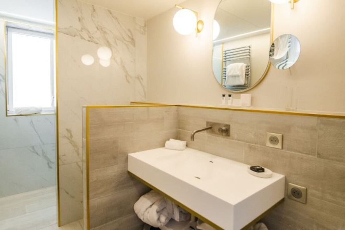 Ein modernes Badezimmer mit einem weißen Waschbecken, Marmorwänden und einem goldfarbenen Spiegelrahmen.