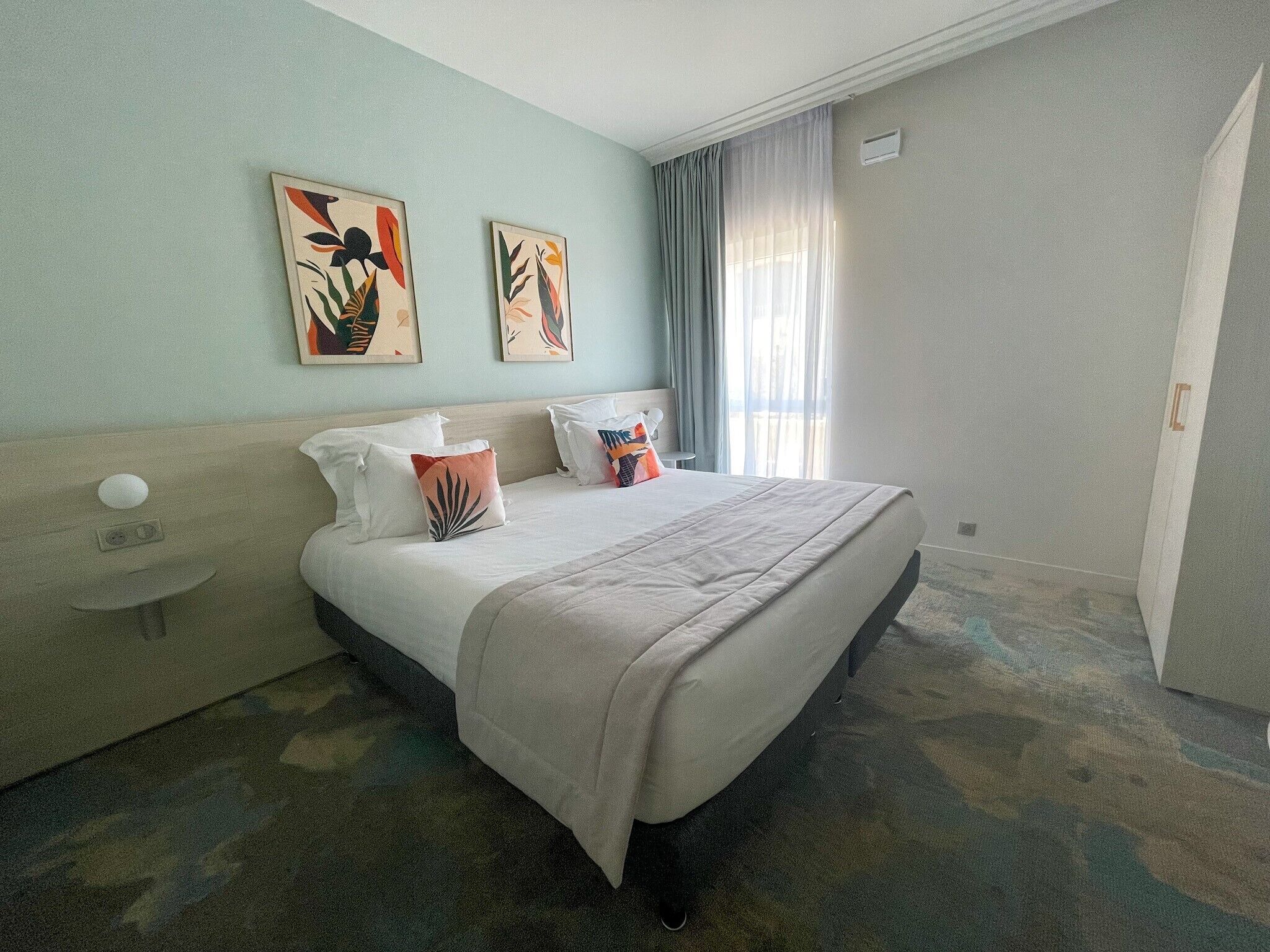 A hotel room with a large bed, a bedside table, and two wall-mounted artworks.