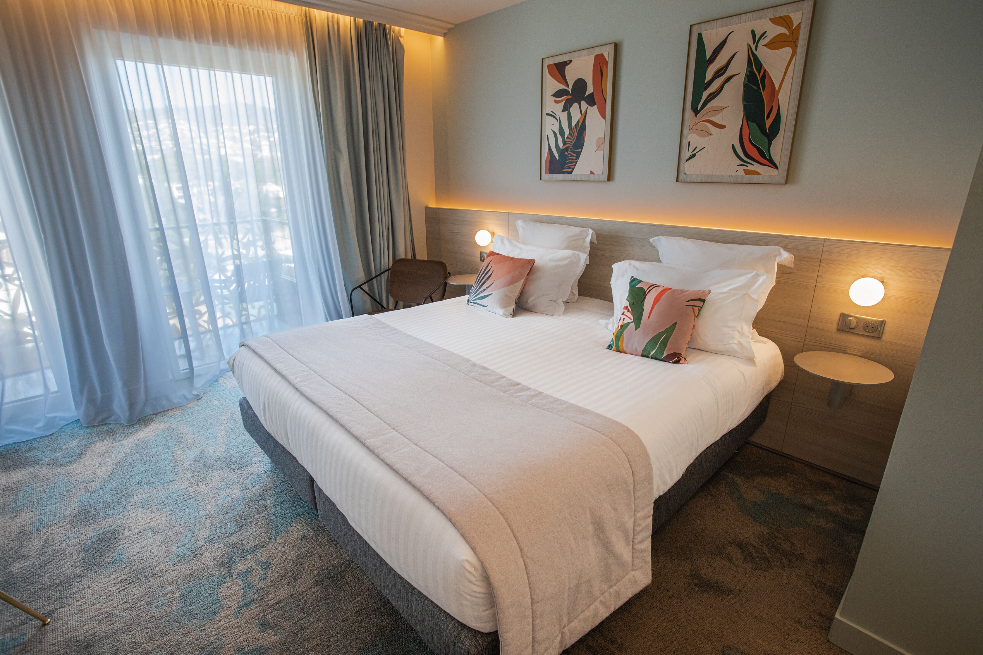 A hotel room with a large bed, two bedside tables, a chair, and a large window with curtains.