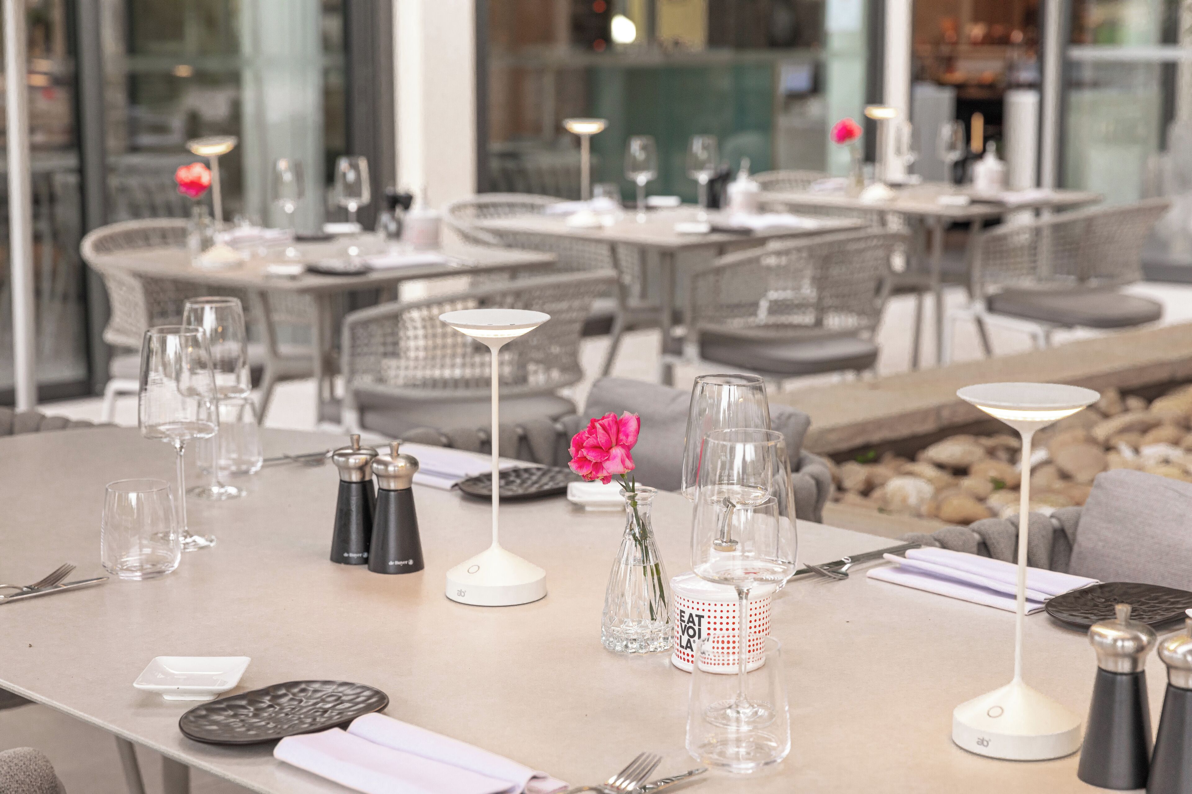 A restaurant setting with tables set for dining, including wine glasses, cutlery, and salt and pepper shakers.