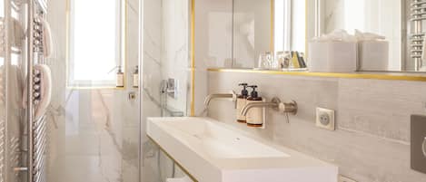A modern bathroom with a glass shower enclosure, a white vanity with gold accents, and a large mirror with integrated lighting.