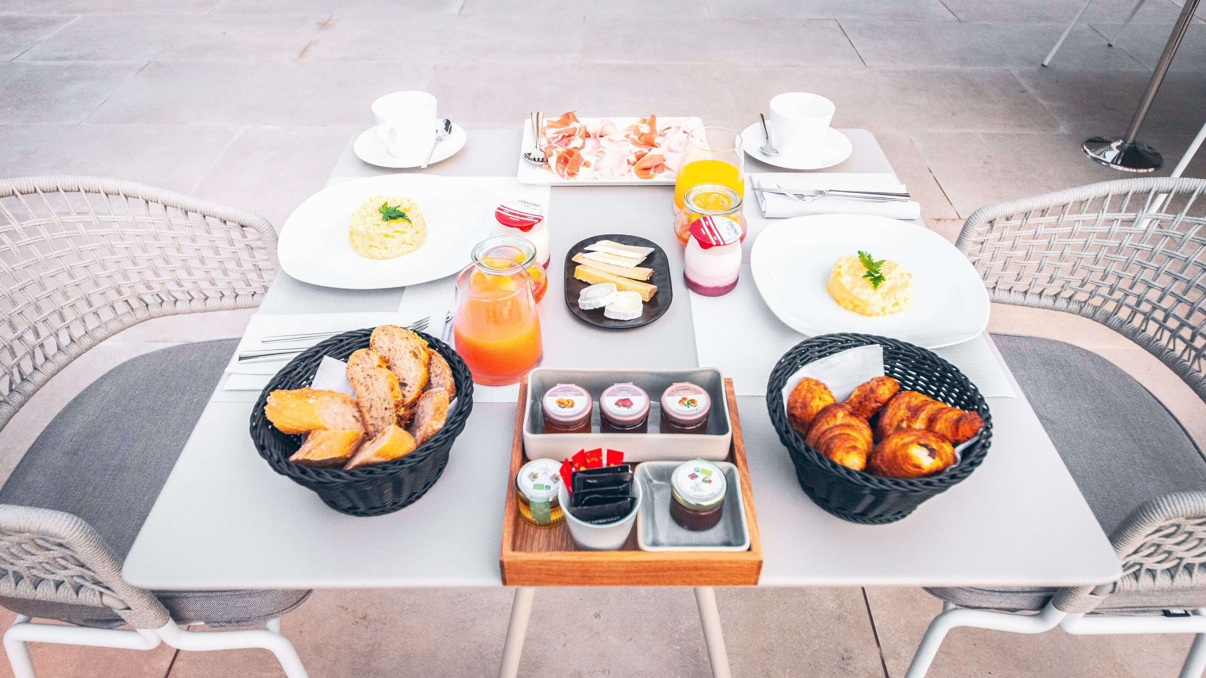 Una mesa preparada para el desayuno con cruasanes, pan, bollería y una bebida de frutas.
