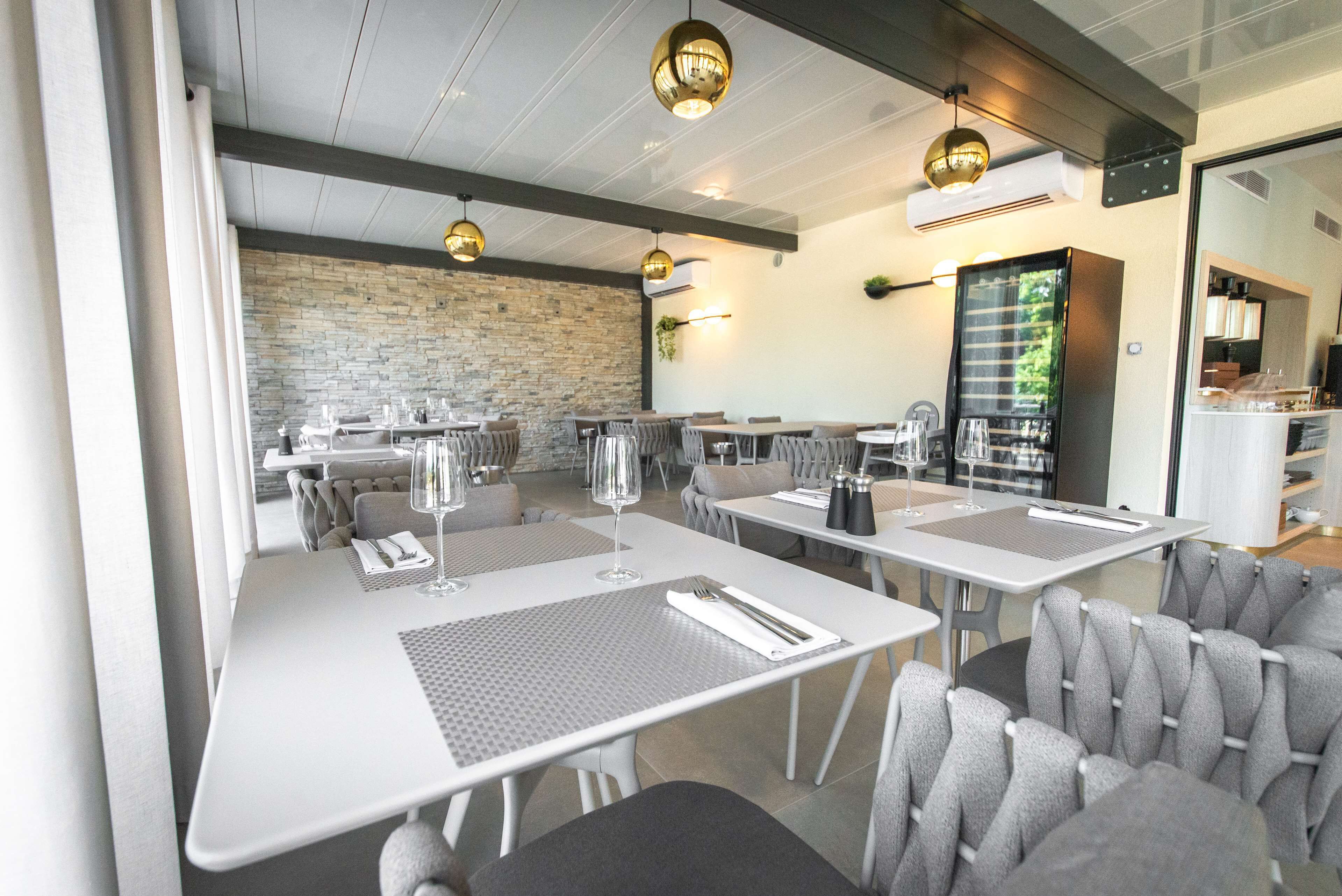 Un restaurant moderne avec des tables blanches, des chaises grises à revêtement et des luminaires suspendus.