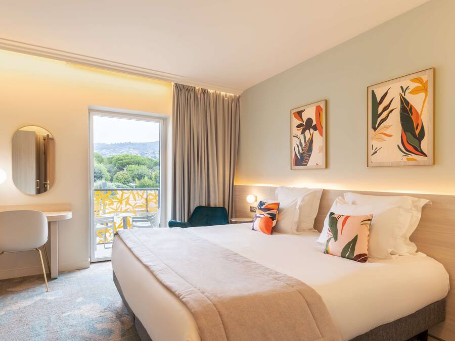 Ein Hotelzimmer mit einem großen Bett, einem Schreibtisch, einem Stuhl und Bildern an den Wänden.