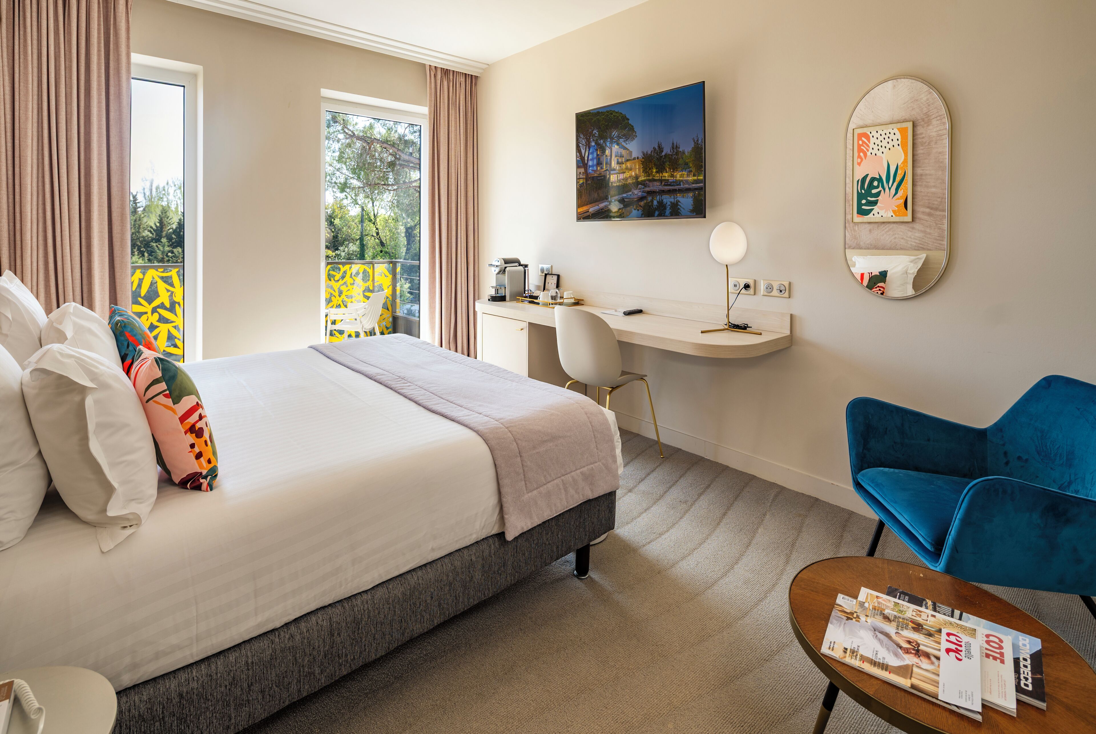A hotel room with a bed, desk, chair, and a small table with magazines.