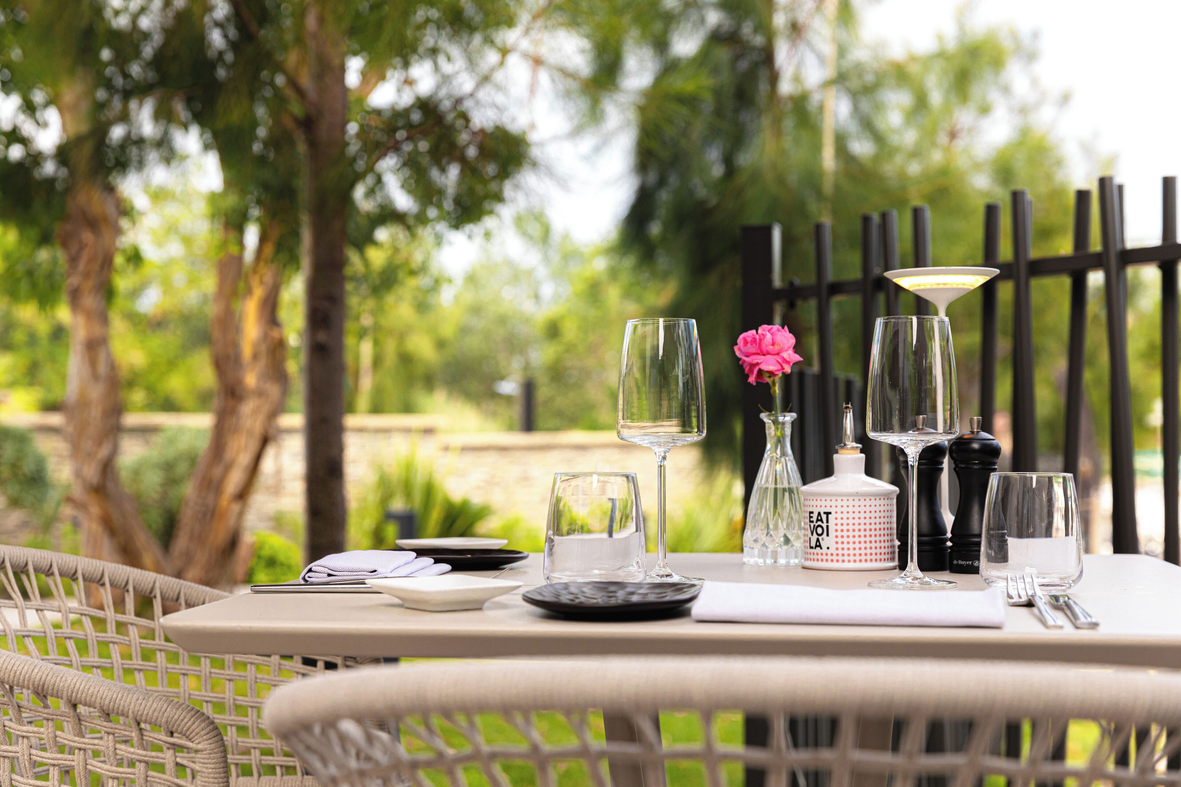 A table set outdoors with a bottle, glasses, and a menu.