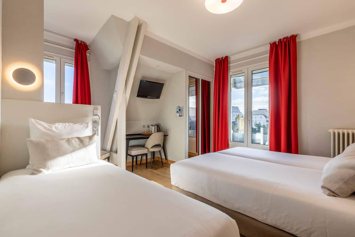 Ein Hotelzimmer mit zwei Betten, einem Schreibtisch, einem Sessel und einem Fernseher.