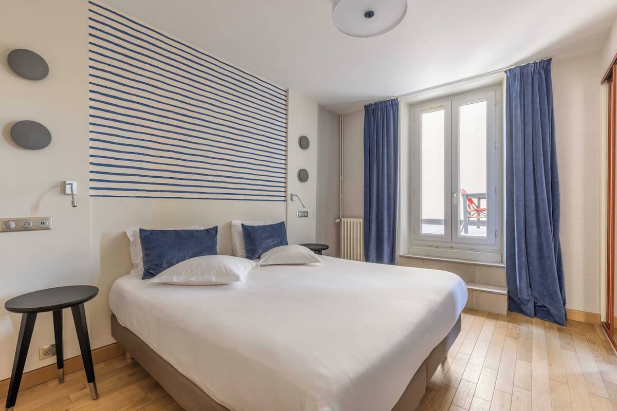 Ein modernes Hotelzimmer mit einem großen Bett, einem kleinen Nachttisch, einem Heizkörper und einem Fenster mit Vorhängen.
