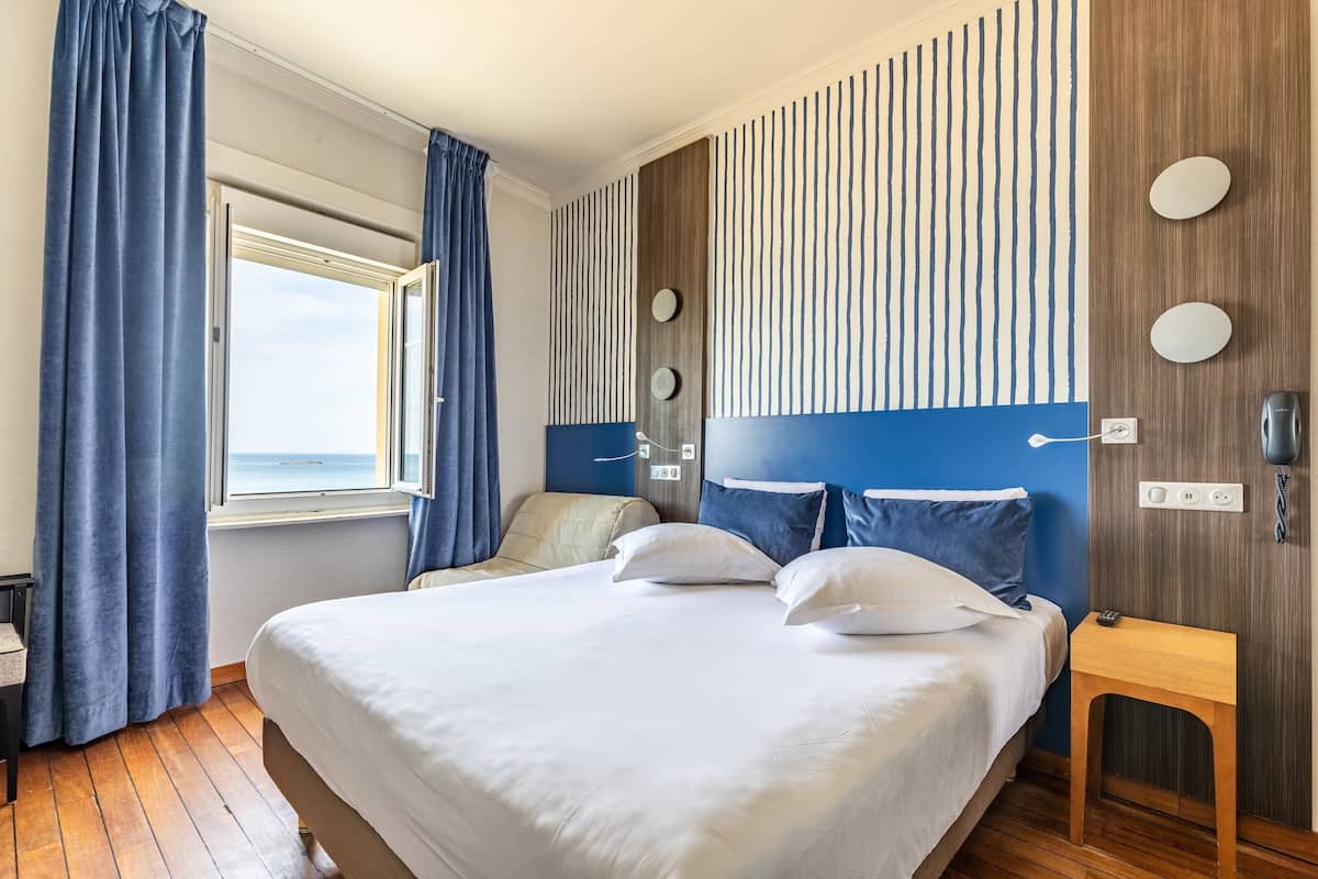 Ein Hotelzimmer mit einem großen Bett, einem Holzkopfschild, Meerblick und einem kleinen Tisch.