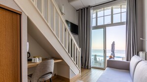 A modern hotel room with a wooden desk, a comfortable sofa, a staircase leading to a balcony with a view of the sea. - Hotel Kyriad Saint Malo centre Plage (Saint-Malo)