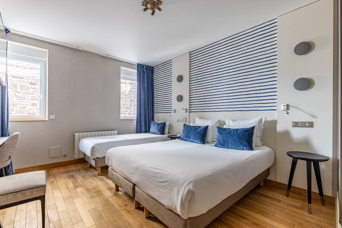 Ein modernes Schlafzimmer mit zwei Betten, einem Sessel, einem kleinen Tisch und einem Fenster mit Vorhängen.