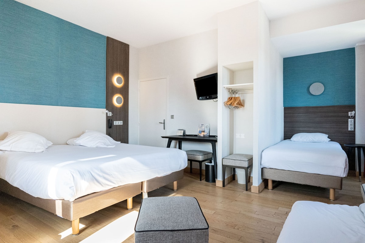Ein Hotelzimmer mit zwei Betten, einem Schreibtisch, einem Fernseher und einer kleinen Sitzecke.