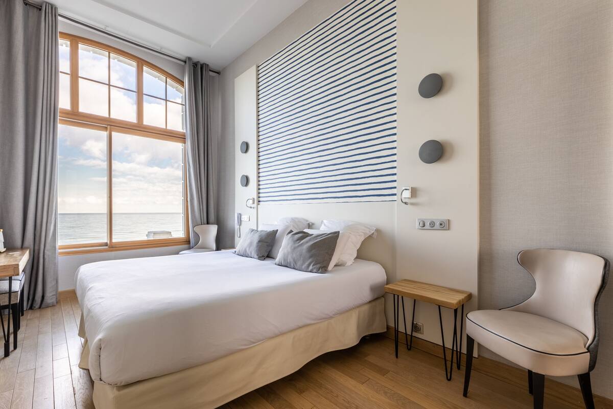 Ein modernes Schlafzimmer mit großem Bett, Meerblick, Schreibtisch und Stuhl.