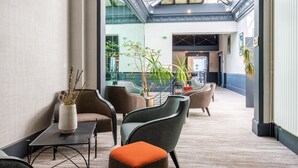 A modern lobby with a glass ceiling, comfortable seating, and indoor plants. - Hotel Kyriad Saint Malo centre Plage (Saint-Malo)