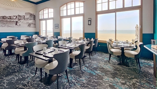 A restaurant with tables and chairs, large windows with a beach view, and a mural on the wall. - Hotel Kyriad Saint Malo centre Plage (Saint-Malo)