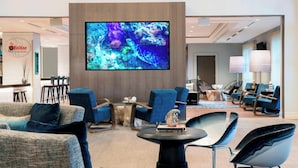 A modern lobby with a large flat-screen TV, blue upholstered chairs, a round table, and a wooden reception desk. - Renaissance Fort Lauderdale Marina Hotel (Fort Lauderdale)