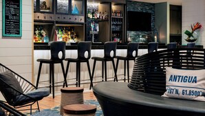 A bar area with multiple stools, a bar counter with various bottles, and a seating area with a cushioned bench and a pillow labeled 'ANTIGUA'. - Renaissance Fort Lauderdale Marina Hotel (Fort Lauderdale)
