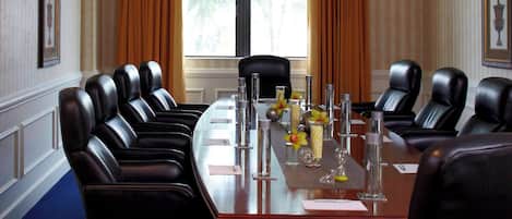 A conference room with a long table, multiple chairs, and a window with curtains.