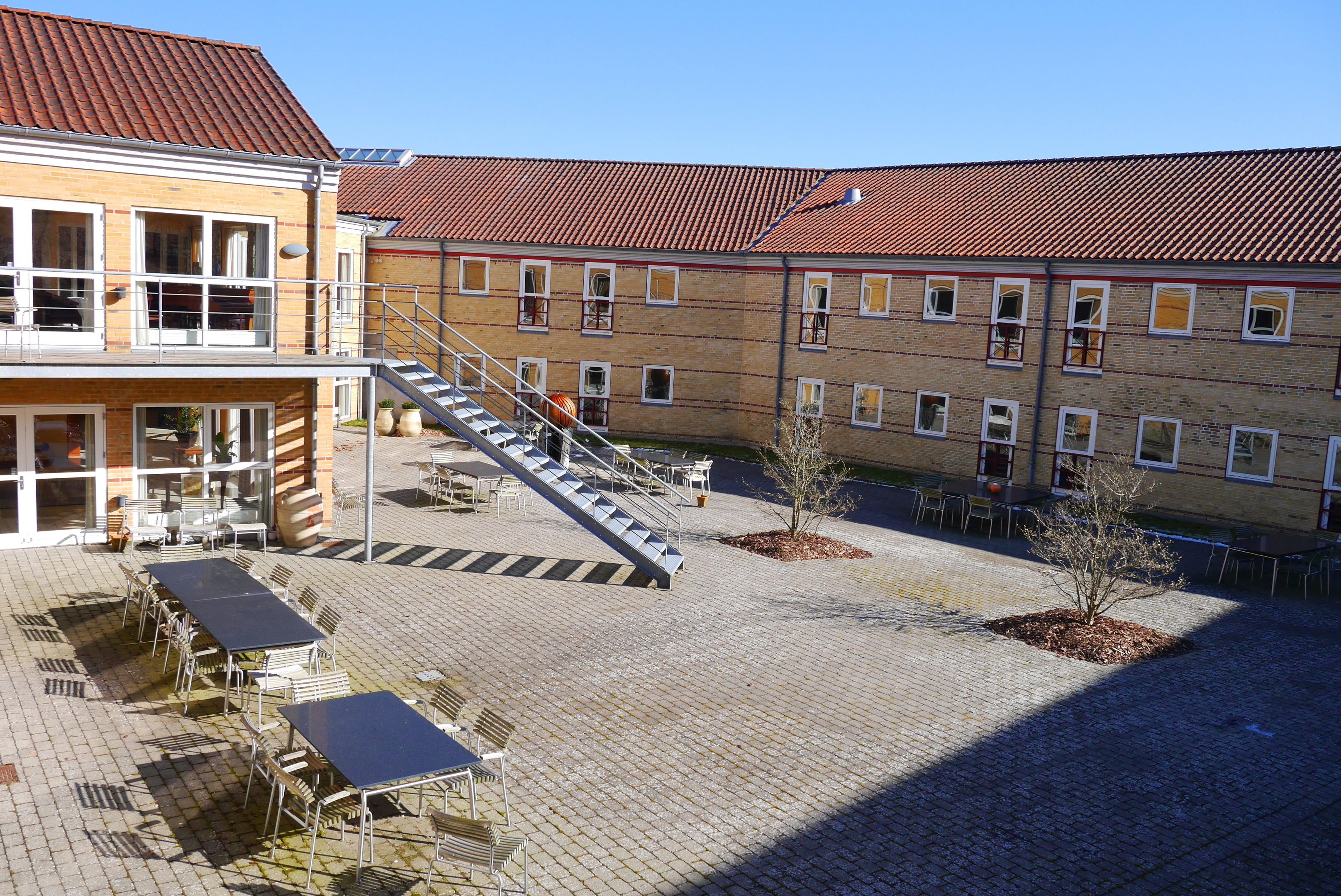 A courtyard with outdoor seating, a staircase, and a building with a red-tiled roof.
