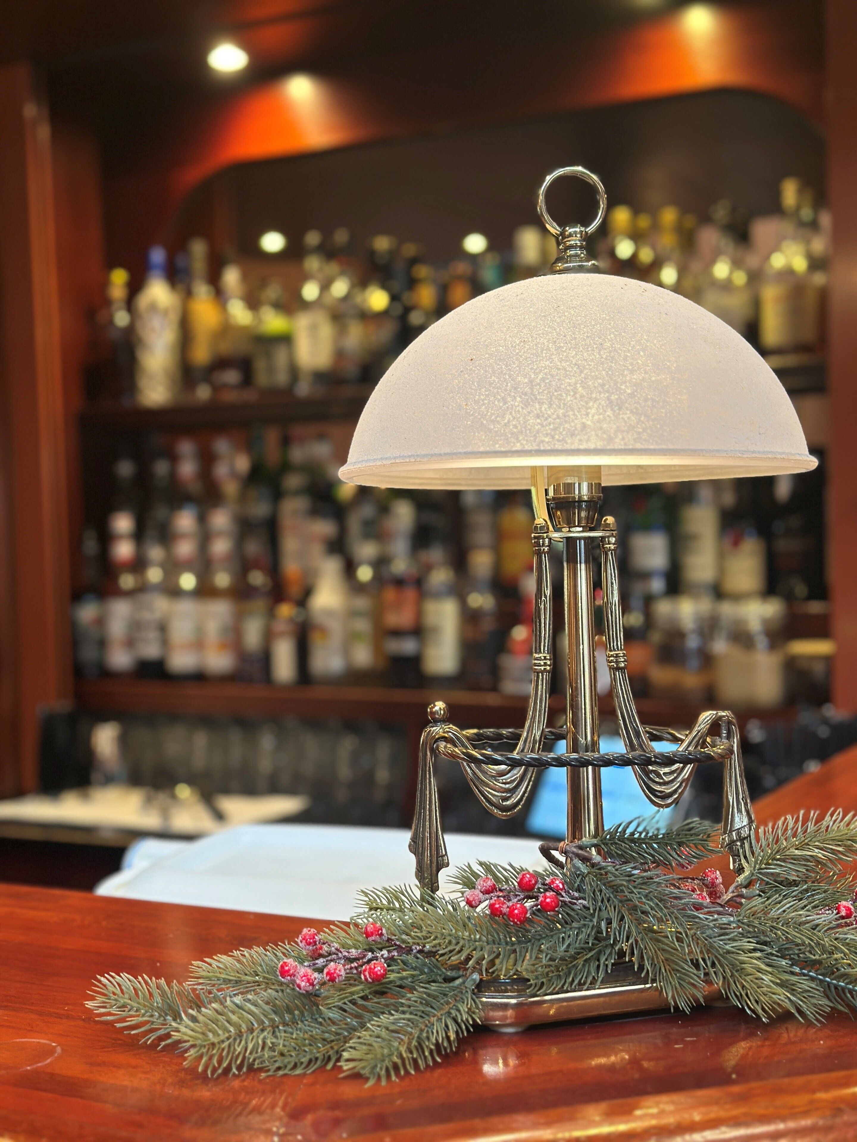 Een bar met een decoratieve lamp, een houten toonbank en een plank met diverse flessen.