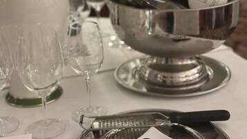 A formal dining table set with silverware, wine glasses, and a silver bowl containing a bottle of wine.