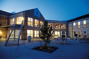 A courtyard with outdoor seating, a staircase, and a building with large windows and a brick facade. - Montra Odder Parkhotel (Odder)