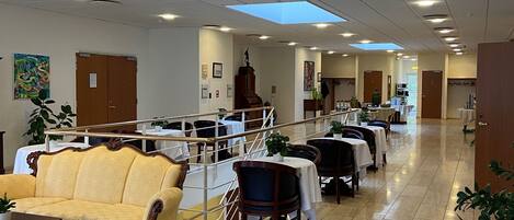 A spacious indoor area with a high ceiling, tiled flooring, and multiple seating arrangements including sofas and tables.