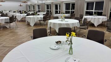 A banquet hall with multiple round tables, each set with white tablecloths, chairs, and small centerpieces.
