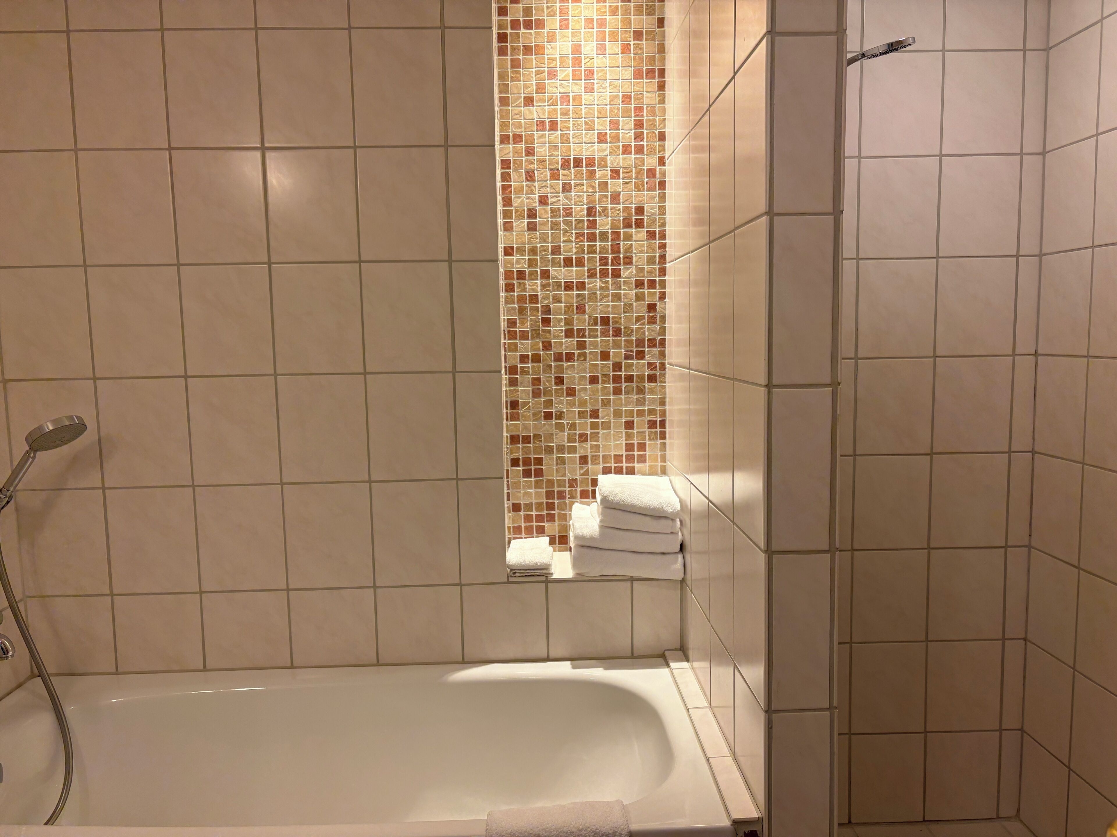 A bathroom with a bathtub, a shower, and a tiled wall with a mosaic pattern.
