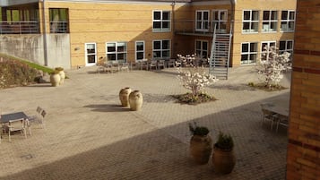 A building with a red-tiled roof, multiple windows, and a paved courtyard with outdoor seating and planters.