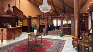 Een ruime lobby met een hoog plafond, gedetailleerd houten meubilair, een grote kroonluchter en een rood, patroonrijk tapijt.