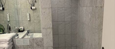 Une salle de bain avec un sol en marbre, un lavabo, des toilettes, une douche avec une serviette suspendue et un miroir avec des lumières.