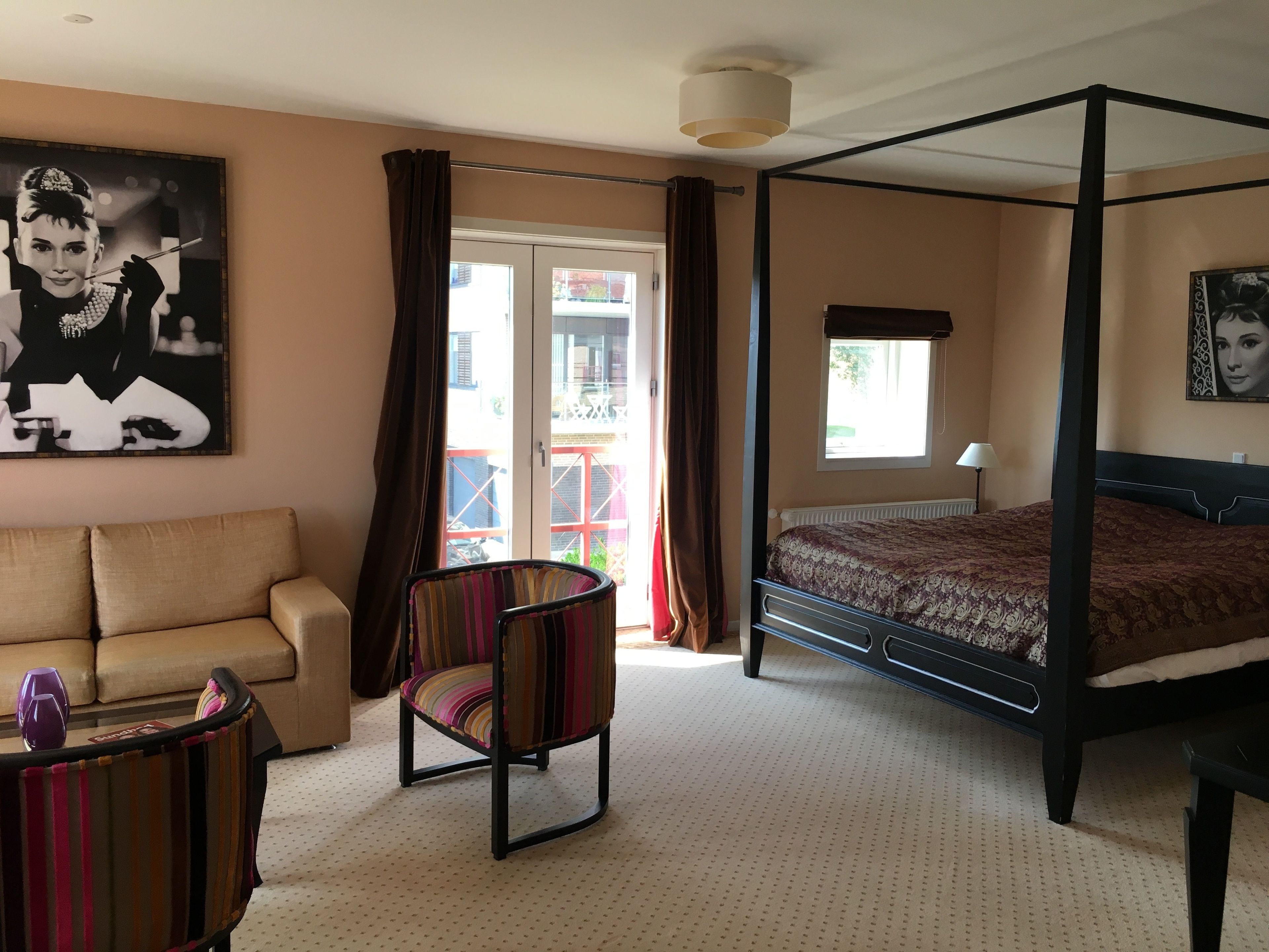 A bedroom with a four-poster bed, a sofa, a striped chair, and a large window with curtains.