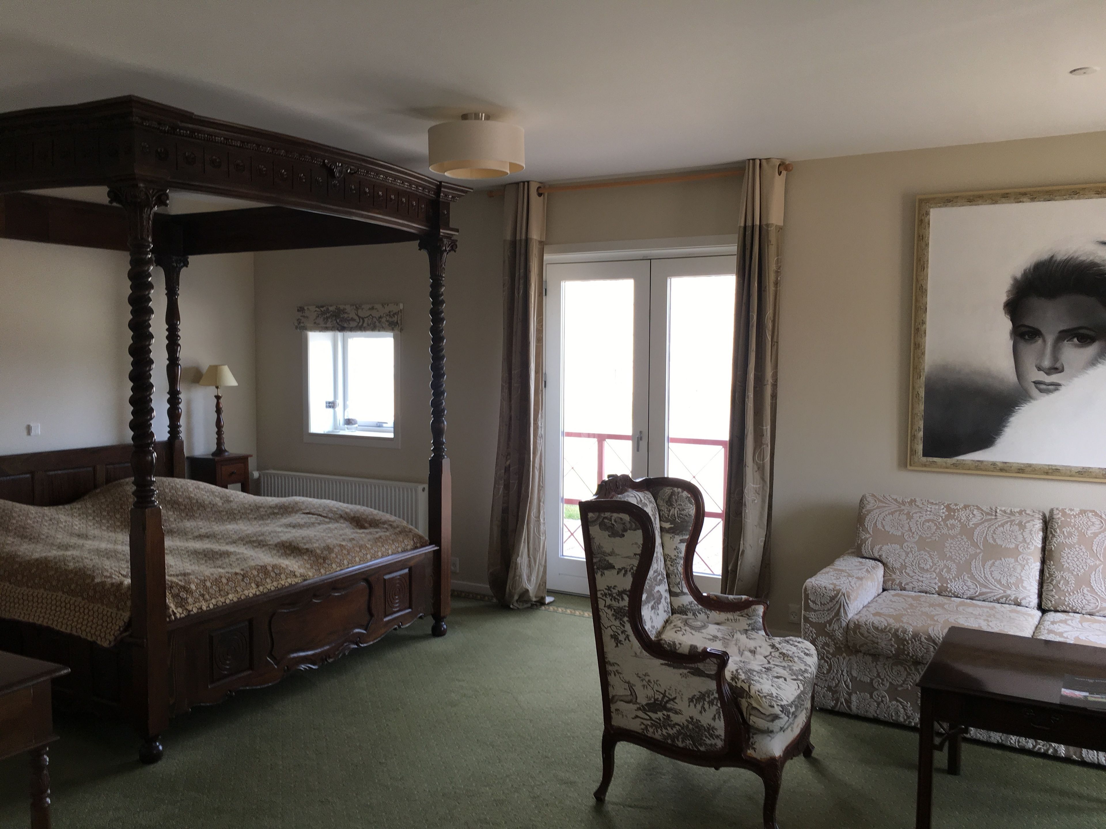 A bedroom with a four-poster bed, a chair, a sofa, and a painting on the wall.