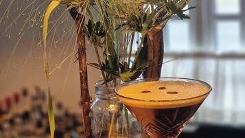 Una copa de martini con espuma, un tarro de vidrio con plantas secas y granos de café esparcidos sobre una mesa.