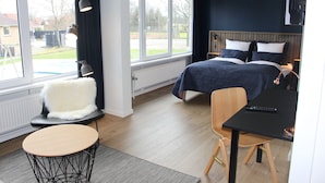 A modern bedroom with a bed, a desk, and a chair. There is a window with curtains and a view of the outside.